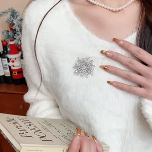 Nahaufnahme einer exquisiten Zirkon-Schneeflocken-Perlenbrosche an einem weißen Flauschipullover.