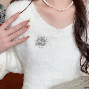 Detailansicht einer eleganten Schneeflocken-Brosche mit Zirkon und Perlen auf weißem Pullover.