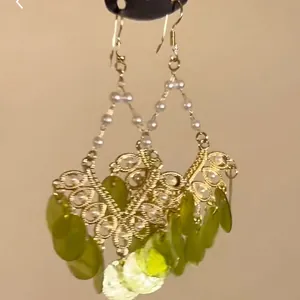 Detailed close-up of ethnic gold hollow earrings with green teardrop pendants and pearls