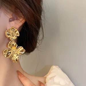 Close-up of large gold flower drop earrings with a textured vintage metallic finish