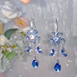 Detailed close-up showing blue floral tassel earrings with butterfly and crystal drops