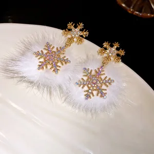 Close-up detail of winter earrings featuring gold snowflakes and white fur balls