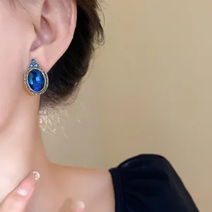 Close-up of a vintage-style blue oval gemstone earring with an elegant gold-tone border