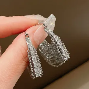 Dettaglio ravvicinato di orecchini a cerchio argento con zirconi e catene a nappe.