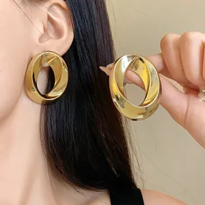 Close-up of chunky gold-tone oval earrings featuring a minimalist twisted metal design