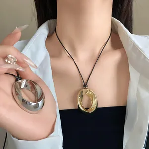 Detail shot of gold and silver twisted oval pendants on black wax cords worn by a model.