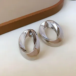 Close-up detail of minimalist silver-tone twisted oval earrings with polished finish