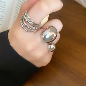 Close-up of silver-tone multi-layered and round bead open rings on a person's hand.