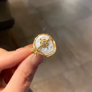 Close-up of elegant baroque pearl ring with golden cross zircon center on finger