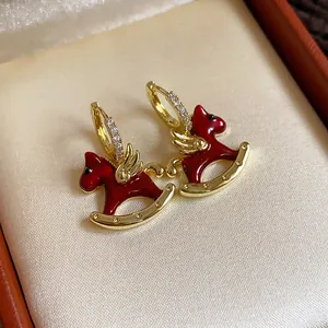 Close-up of red enamel rocking horse charms on zircon-studded gold hoop earrings
