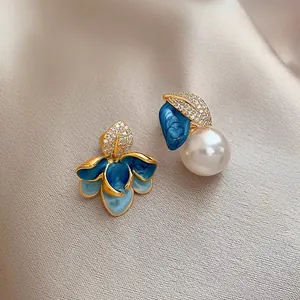 Close-up detail of vintage asymmetric blue enamel flower and large pearl stud earrings