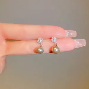 Close-up of zircon flower pearl drop earrings held between fingers showing fine details.