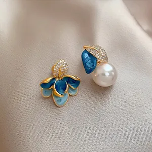 Detail view of asymmetric blue enamel floral earrings with a white pearl and gold plating