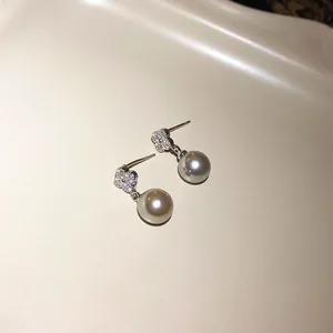 Close-up detail of elegant silver needle earrings with zircon flower and pearl drop