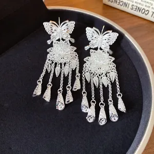 Détail des boucles d'oreilles papillon et fleur en argent avec pompons et clochettes.