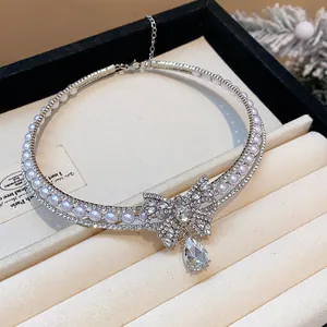 Close-up of sparkling zircon and pearl choker necklace with a large bow pendant.