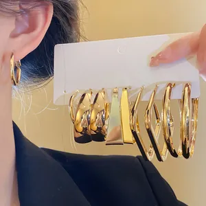 Close-up detail of stylish gold geometric hoop and stud earrings set on a white card