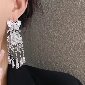 Détail de boucles d'oreilles papillon et fleur avec pampilles et texture filigrane.