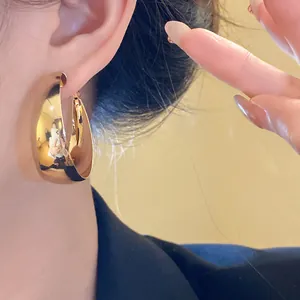Detailed close-up view of a minimalist gold wide hoop earring worn on a woman's ear