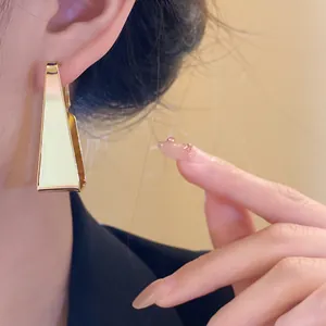 Detailed close-up of minimalist gold geometric trapezoid earrings worn on model's ear