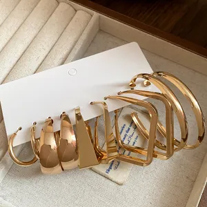 Close-up detail of several pairs of gold geometric hoop earrings on a white card