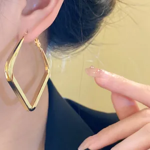 Close-up of elegant large gold geometric rhombus hoop earrings worn for a stylish look