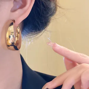 Close-up view of elegant chunky gold hoop earrings with mirror finish worn on ear