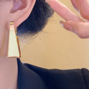 Detail view of gold-tone geometric trapezoidal earrings worn by model for elegant style