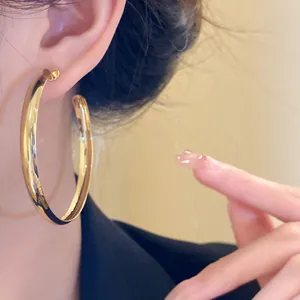 Close-up view of elegant thick gold hoop earrings with silver needles on model's ear
