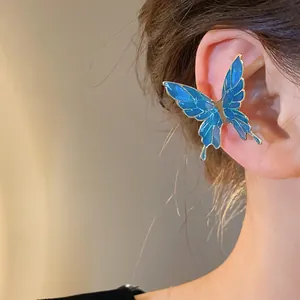Elegant close-up of a blue enamel butterfly ear cuff worn on an ear for a stylish look.