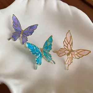 Close-up of three colorful butterfly oil-drip ear clips on a white shell ceramic tray