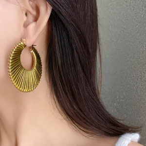 Detailed view of gold textured hoop earrings worn on ear showing pleated design