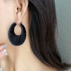 Close-up detail of large black pleated hoop earring showing intricate woven texture on model