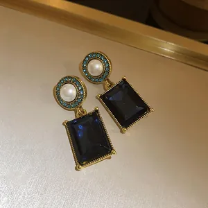 Macro detail of vintage style gold earrings featuring pearls and rectangular blue gems