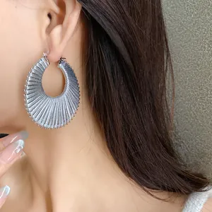 Detailed close-up view of a large silver textured hoop earring worn on a model's ear