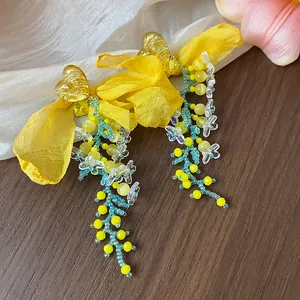 Close-up detail of sweet yellow chiffon bow drop earrings with heart studs and beads.
