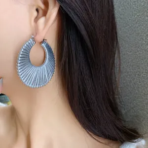 Close-up of silver fan-shaped hoop earrings with metallic ribbed texture on model