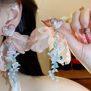 Close-up detail of pink heart chiffon bow and beaded floral dangle earrings on model.