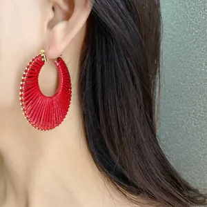 Close-up of vibrant red woven hoop earring with gold bead trim on an Asian model.
