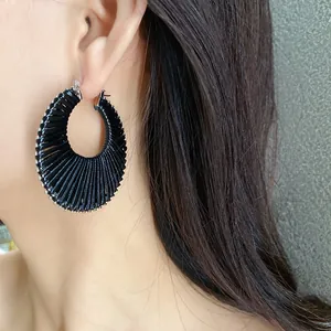 Close-up view of a stylish black woven hoop earring worn by a model in a natural setting