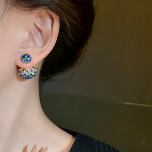 Close-up of elegant double-sided stud earrings featuring blue and white crystals on an ear