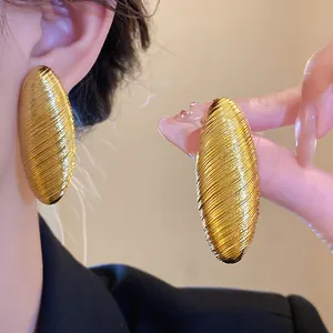 Close-up of large textured golden oval stud earrings with retro vintage metallic finish