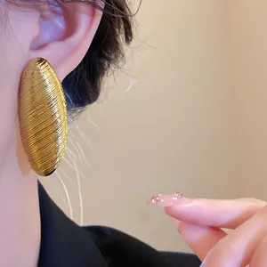 Close-up of a vintage gold oval ribbed ear stud on a model with detailed texture