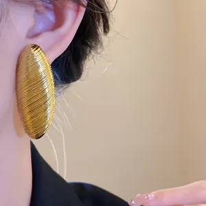 High-quality detail shot of vintage textured golden oval stud earrings on an ear model