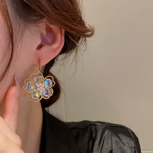 Detailansicht der goldenen Blumenohrringe mit Kristallen und Perlen an einem Modell.