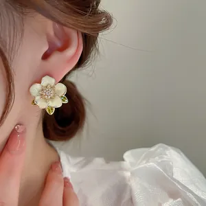 Detaillierte Nahaufnahme eleganter weißer Perlenblumen-Ohrstecker mit grünen Blättern