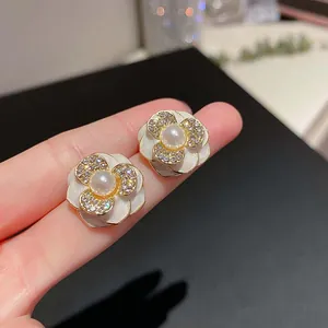 Nahaufnahme weißer Emaille-Ohrstecker in Blumenform mit Perle und Strasssteinen