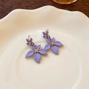 Dettaglio di orecchini a pendente con fiori viola opaco su un piatto di ceramica bianca.