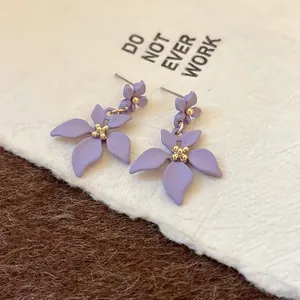 Dettaglio di orecchini a doppia goccia di fiori viola opaco su cartoncino bianco testurizzato.