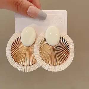 Dettaglio di orecchini retrò in rafia intrecciata a forma di ventaglio con perni ovali.